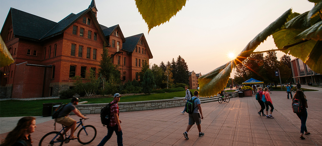 Students walk in front of Montana Hall during sunrise.