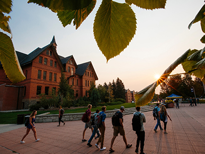 Students walk in front of Montana Hall during sunrise