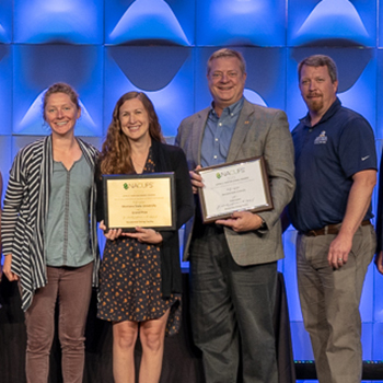 four staff members smiling and holding two award plaques