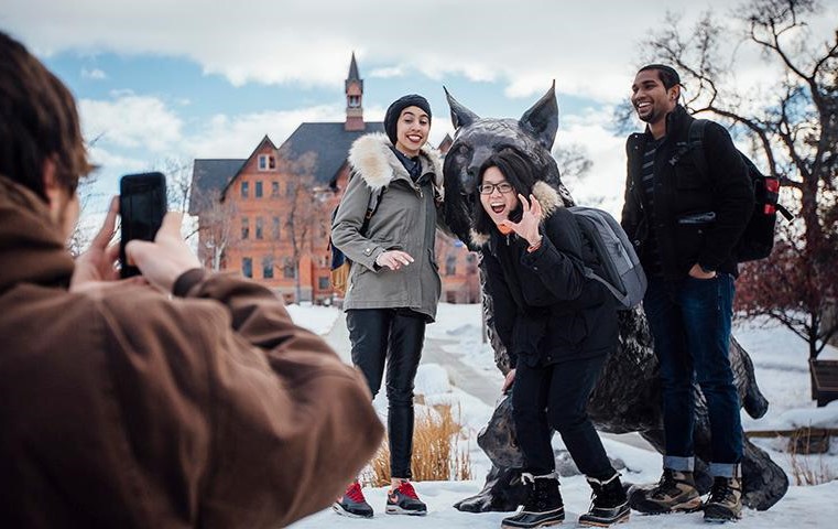3 international students smiling and posing for a picture at the bobcat statue