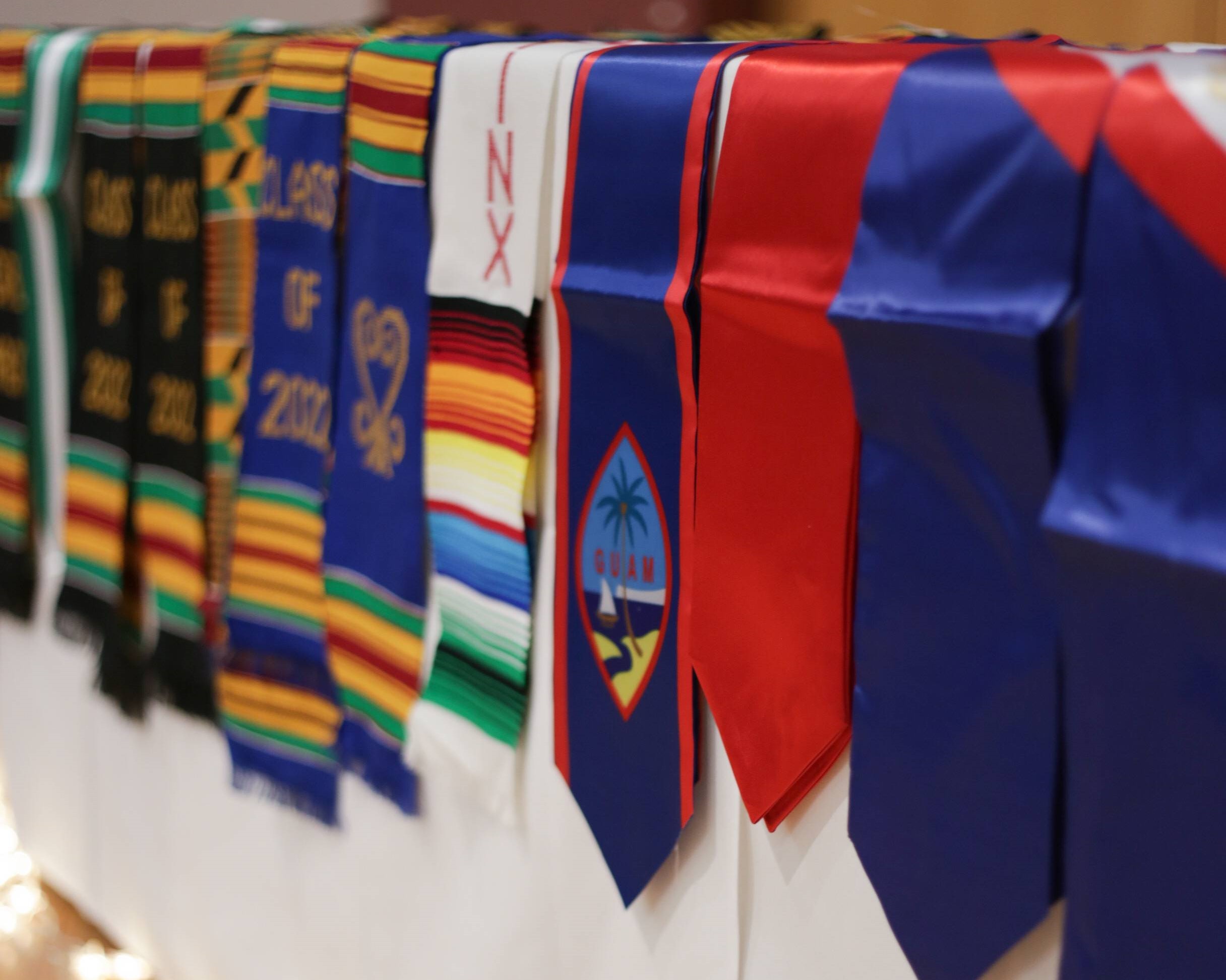 Multicultural Graduation stoles lined up side-by-side hanging off the edge of a table