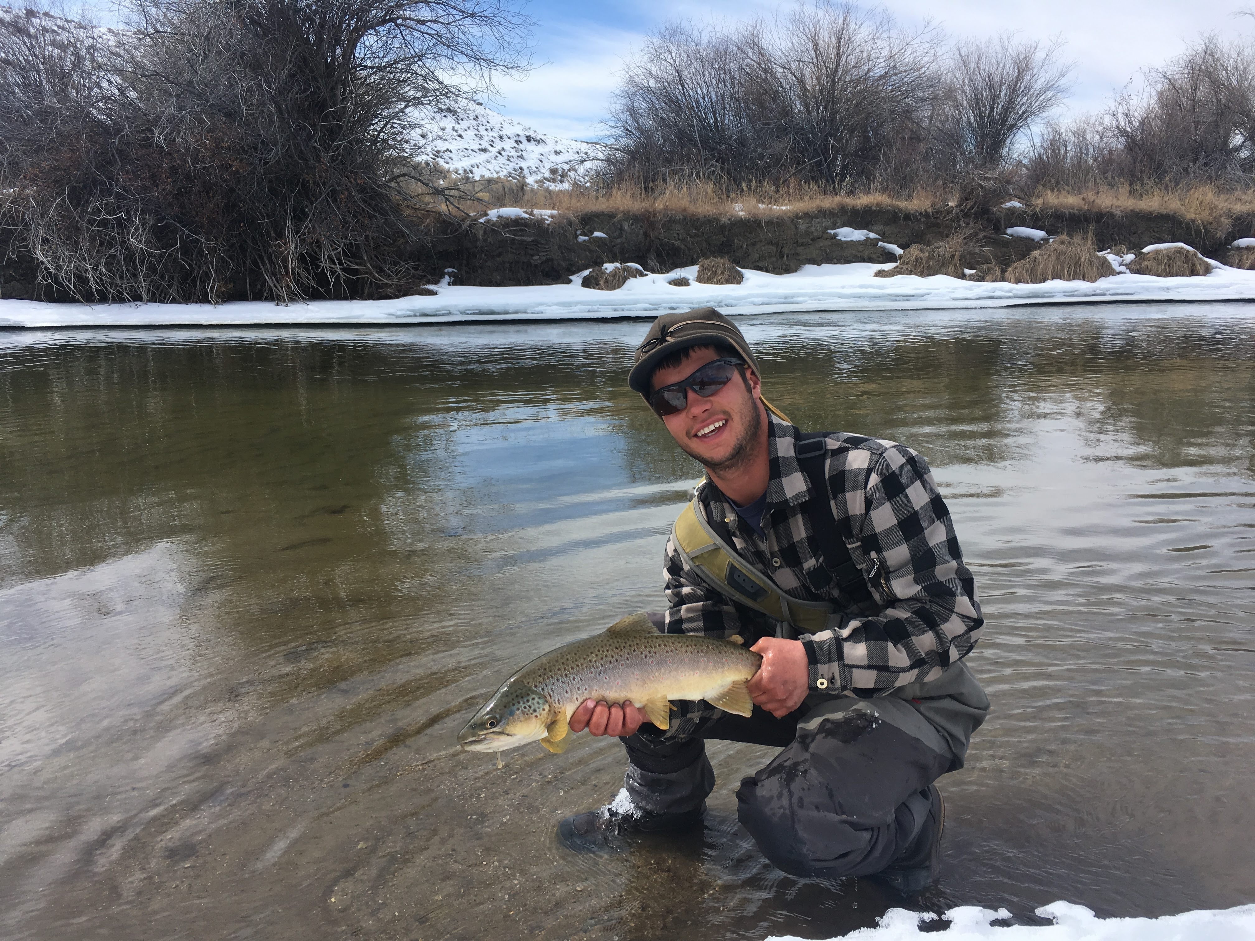 Colter Brown kneels in stream holding a brown trout