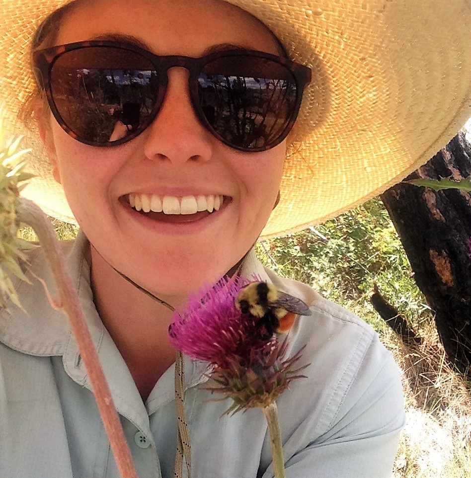 Simone smiling holding purple flower with a bee on it