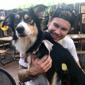 Adam Hrabovsky Adam Hrabovsky holds a black, white, and tan dog in a restaurant's outdoor seating area