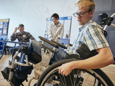photo of student in wheelchair he designed with two students in background