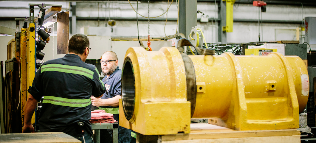 Two workers at manufacturing plan with large yellow metal part in foreground