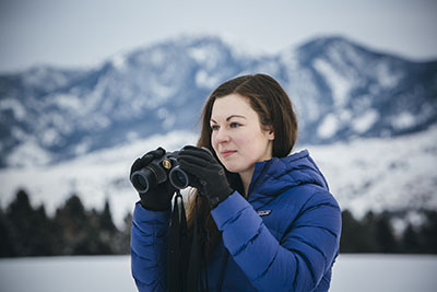 Elizabeth Flesch looks through binoculars in front of snowy mountains