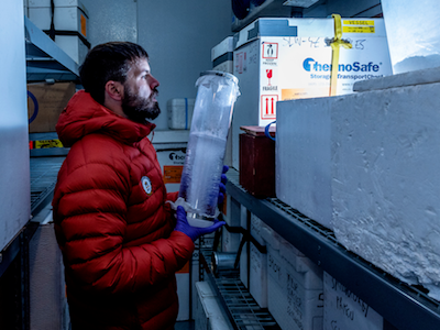 MSU researcher in orange puffy coat handling cylindrical ice core sample