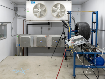 cold room with concrete floor, including experiment in which blue rack holds car tire that spins