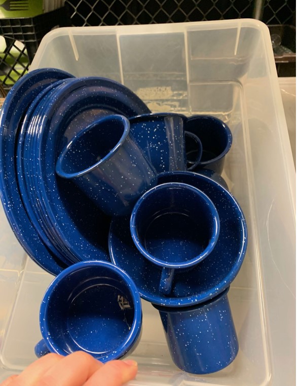 Tub filled with blue metal camp dishes and mugs