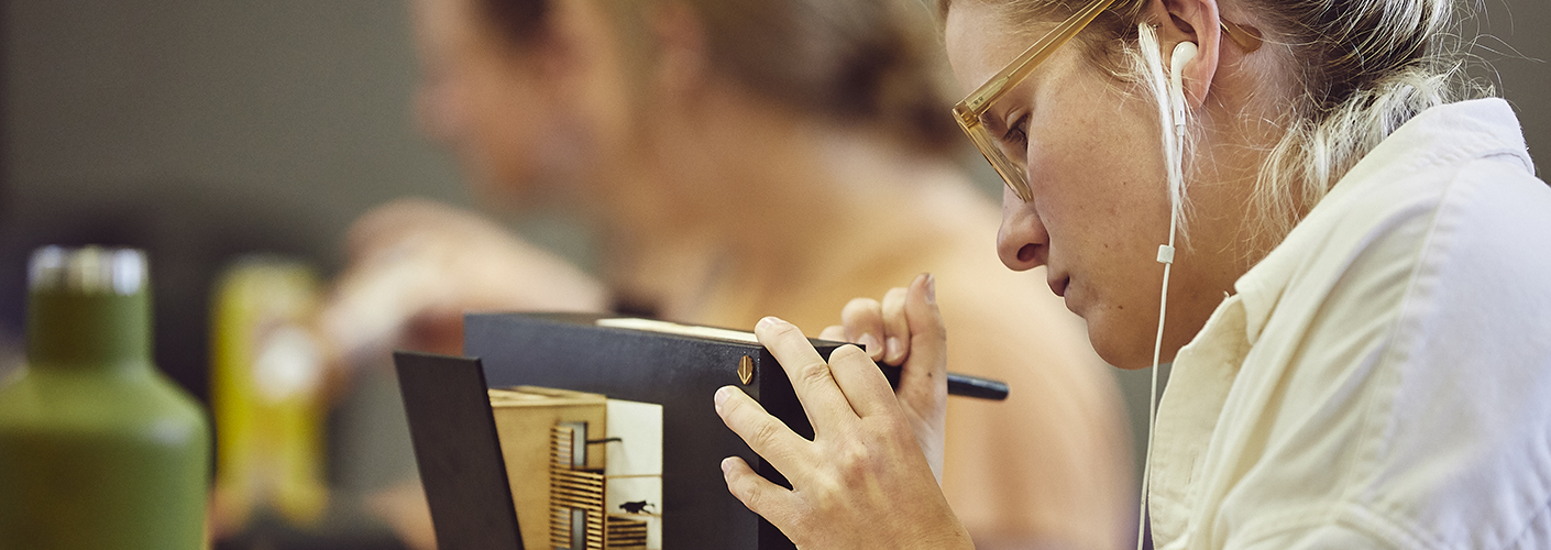 A young Caucasian woman makes last-minute adjustments to an architectural model.