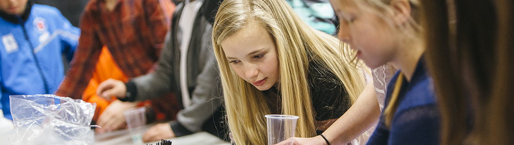 A group of young students intently lean over an experiment in progress.