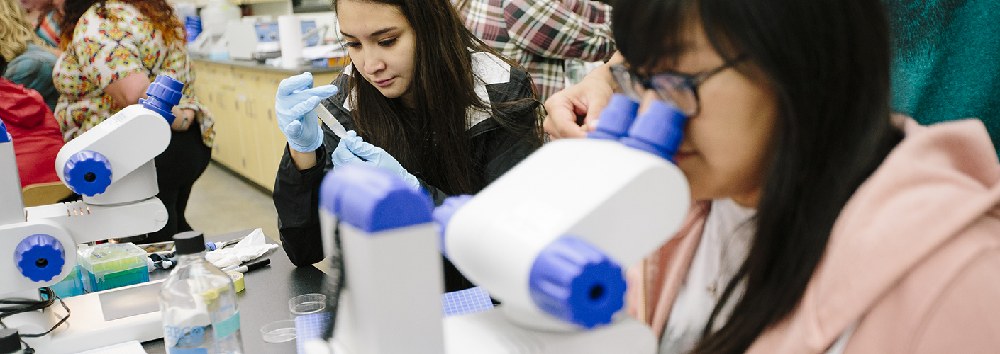Two young women inspect cellular material in microscopes.