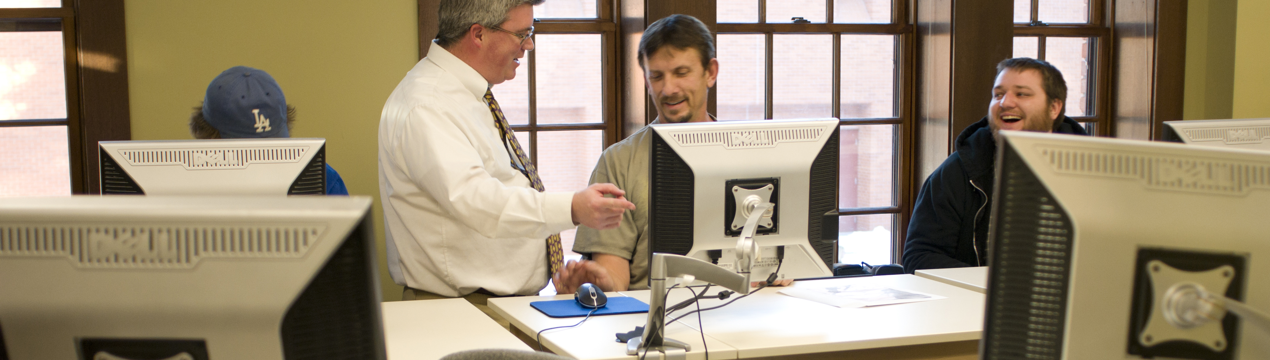 A man in a baseball cap renders a drawing in CAD software, the illustration displaying on a computer screen.