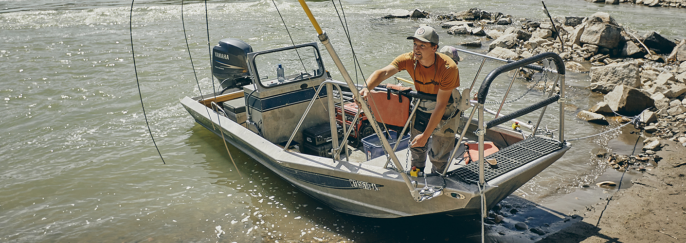 A man stands on a boat as it is moored ashore on the Yellowstone River.