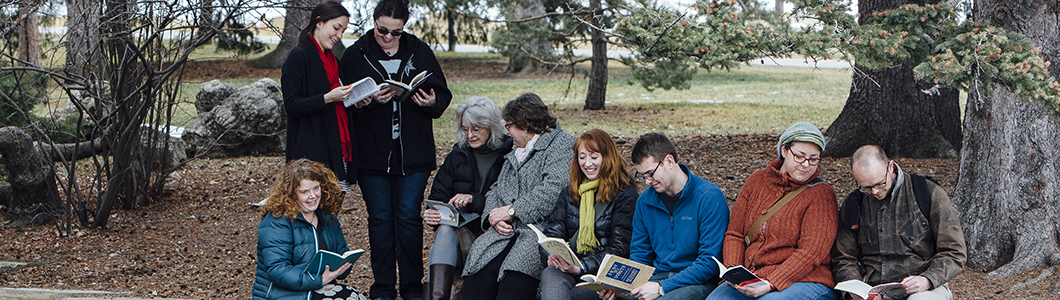 A group of students read and discuss a text by the Duck Pond on campus.