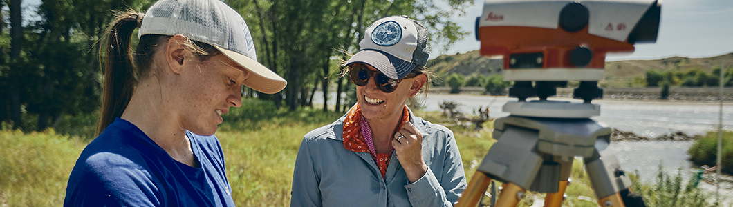 Two women with surveying equipment on a river bank