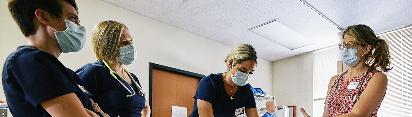 Two women, one with curly gray hair and the other with long dark hair, discuss a training module while in PPE.