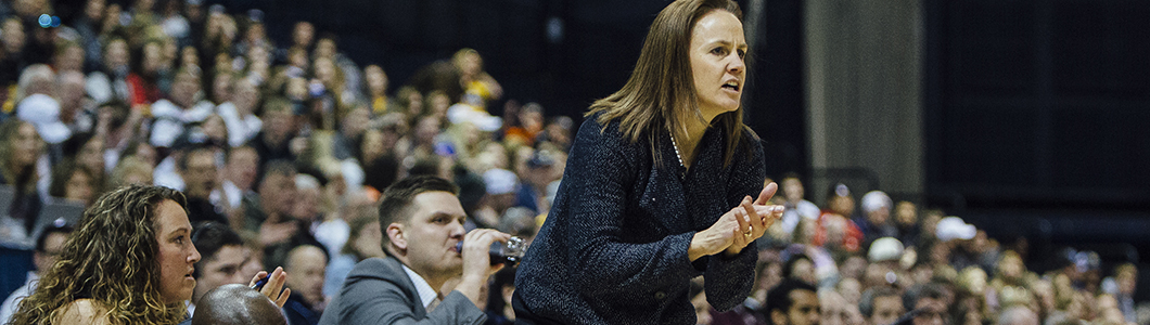 A woman cheers her student athletes on from the sidelines of an arena.