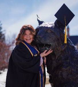 Picture of Emily Cappis in a graduation gown next to the Spirit Statue on MSU's campus
