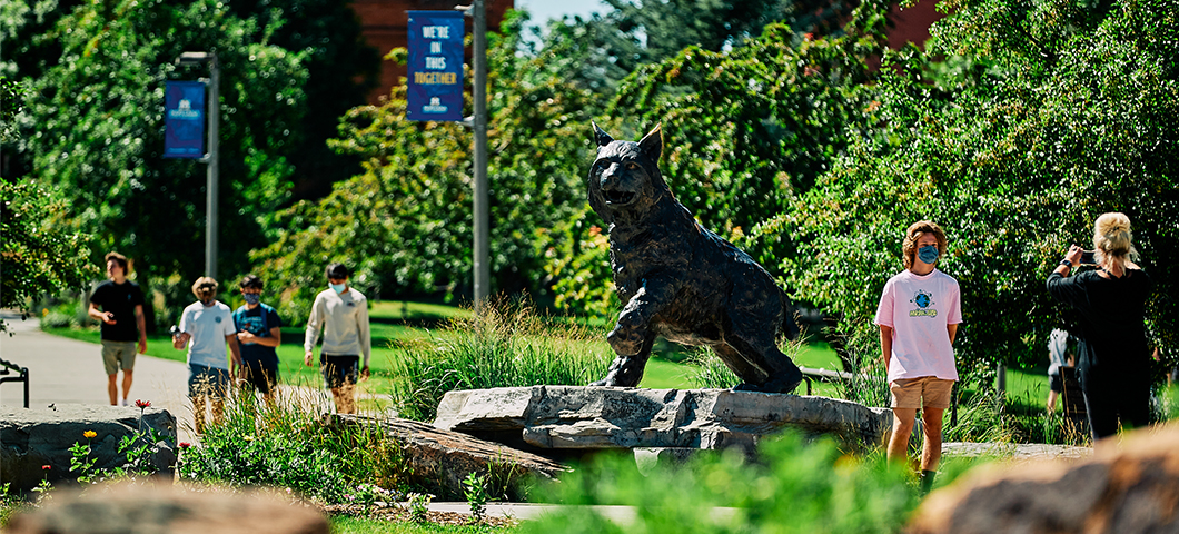 A student takes a photo in front of the Bobcat statue with a mask on.