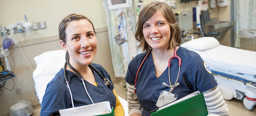 Two nursing students stand in a simulator.