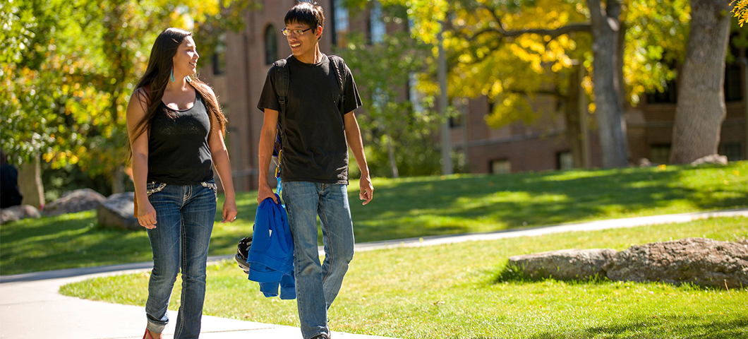 Two students walking in front of Montana Hall in fall.