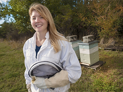 Laura Brutscher poses in her beekeeping gear next to a hive