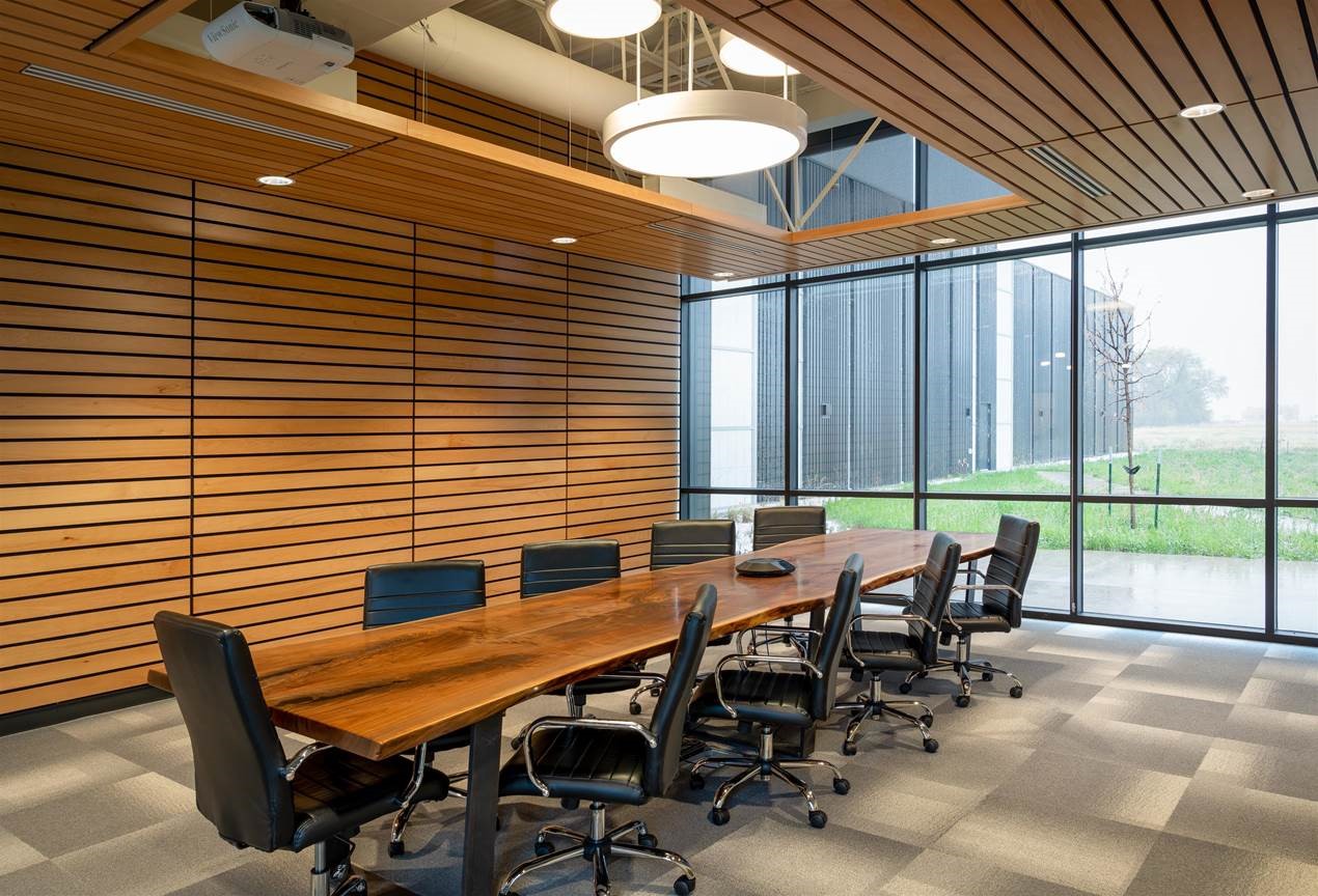 Conference room space, with wood slatted walls, and a large wooden table in the middle. Chairs surround the table.