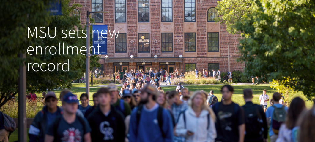 Students walk along a sidewalk on a college campus. A brick building is in the background. | MSU