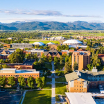Aerial view of a college campus during summer with mountains on the horizon in the background beneath a blue sky.