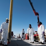 A gravity core is hoisted by a crane arm above the borehole at the Mercer Subglacial Lake in Antarctica as several scientist and crew look on.. 