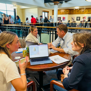 A group of students and mentors discuss portfolios at many tables