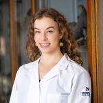 Ingrid Peters wearing an MSU logo lab jacket standing by a display case 