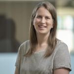 a woman in a striped shirt smiles at the camera in front of an out of focus background