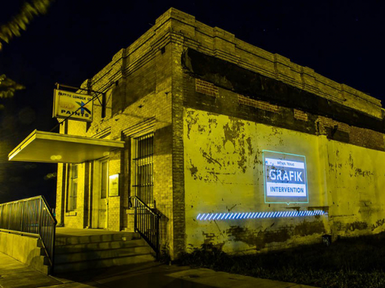 A projection with the words Grafik Intervention is displayed on the side of a building at night | 