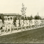 Historic image of dozens of women walking on a sidewalk on campus.