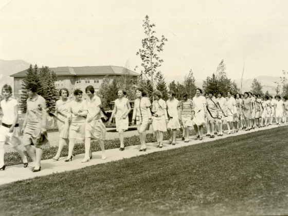 Historic image of dozens of women walking on a sidewalk on campus. | 