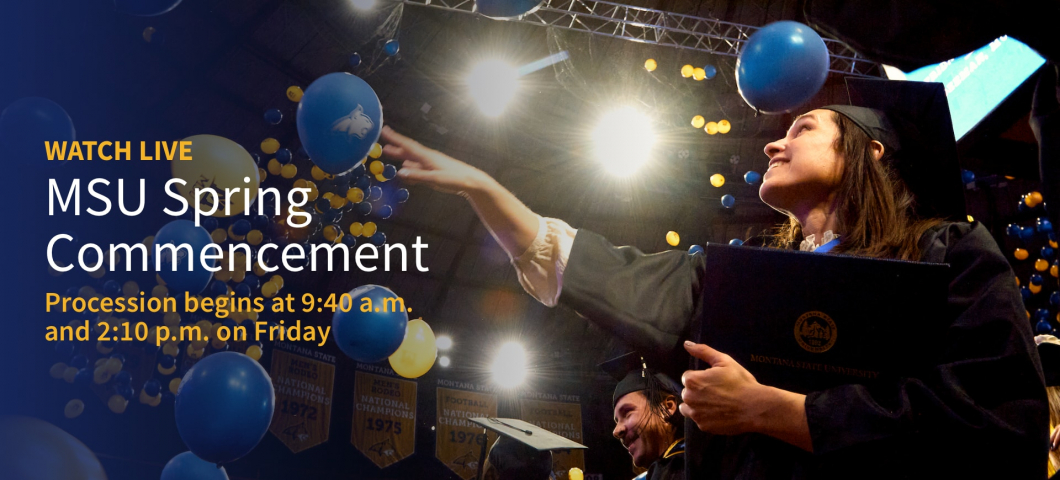 Alt text: A smiling graduate in a black cap and gown holds a Montana State University diploma cover and reaches toward the air as blue and yellow balloons fall around her during a commencement ceremony. The background shows bright lights, celebratory bann | MSU