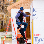 Men lean on a ladder and look at the frame of a building
