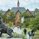 A landscape view of Montana Hall with a statue of a bobcat in the foreground.
