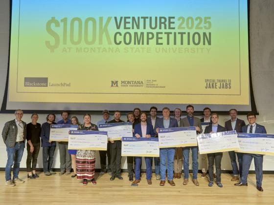 A large group stands in front of a projection screen holding large, fake checks. | MSU photo by Colter Peterson