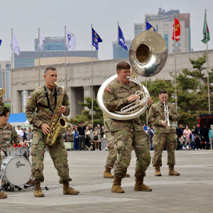 A group of people wearing U.S. Army uniforms performing music with brass instruments in a public area.