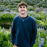 Miles Sumner is photographed in front of a field of lupines. 