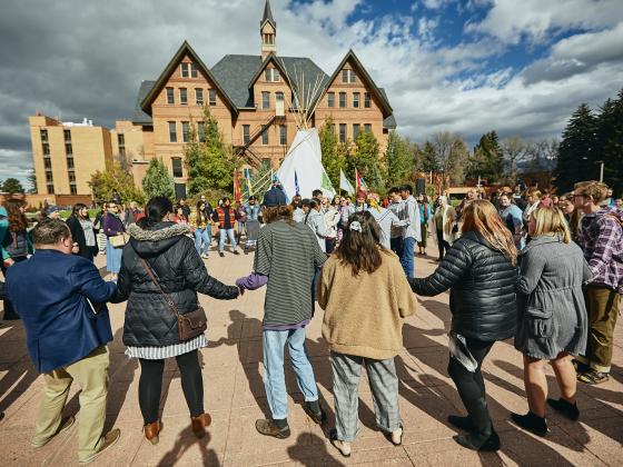 A group of people holding hands with Montana Hall in the background | MSU photo by Adrian Sanchez-Gonzalez