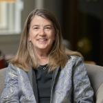 Liz Shanahan sits on an armchair looking at the camera in front of an out of focus background