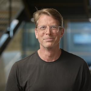A man stands in front of an out of focus background, smiling at the camera