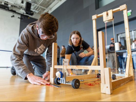 Two young students set up a device with wheels on the floor of a large room. | MSU photo by Marcus "Doc" Cravens
