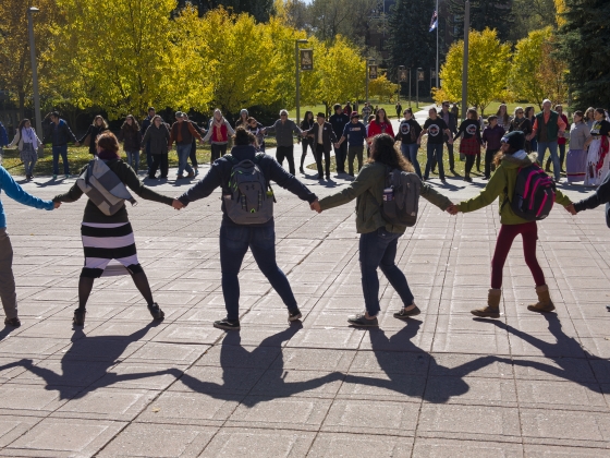 A wide view of people holding hands and dancing in a large circle | MSU Photo by Kelly Gorham