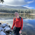 Vanessa poses for a photo in front of a mountain lake. 